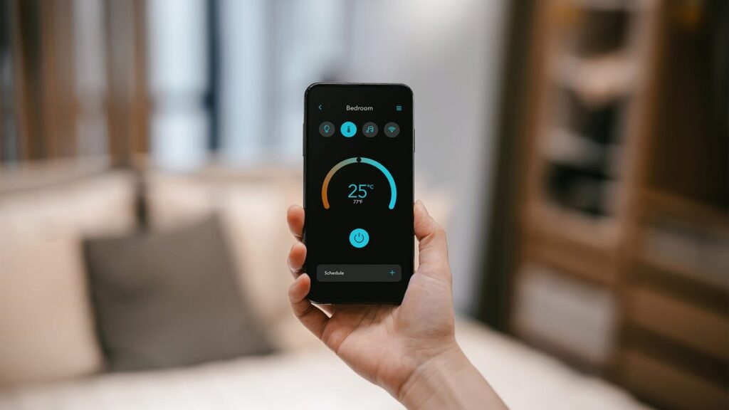 Close-up of a woman's hand holding a smartphone and setting up the smart home system, remote control of the smart air conditioner's thermostat in the living room of her smart home.  Smart life.  Lifestyle and Technology - Stock Photo